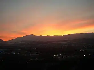 Sunset lights up the sky, silhouetting a long, notched ridge with a prominent peak toward its left-hand (southern) end.