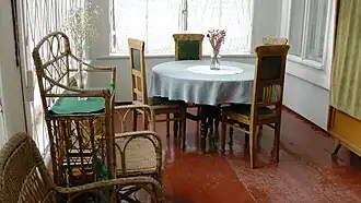 An interior porch with a lot of light, a round table with a vase on it, four chairs, and some other pieces of rustic furniture.