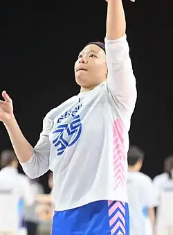 A woman in sports clothes jumping, her left hand in the air.