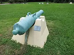 Cannon with green patina mounted on a concrete pedestal.