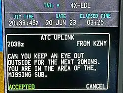 Digital display showing the aircraft registration, the date, the time in UTC "20:38:43z", and the text 'Can you keep an eye out outside for the next 20mins, you are in the area of the missing sub.'