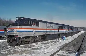 A gray diesel locomotive with a black roof. On the side are red, white, and blue stripes of equal width.
