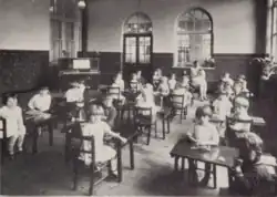 Young children seated at tables in a school classroom.