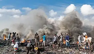 Several people are working on a heap of rubbish, with smoke rising from it.