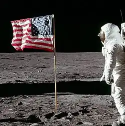 Cropped photo of Buzz Aldrin saluting the flag. The fingers of Aldrin's right hand can be seen behind his helmet, next to his visor.