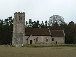 A stone church with red tiled roofs seen from the south, showing a battlemented tower, a nave with a south porch, and a chancel at a lower level