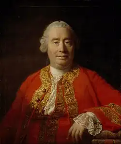 Oil painting showing a man from the front against a dark background, dressed in a red coat with gold embroidery, his left arm resting on a surface