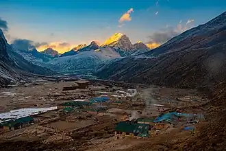 A village in a large mountain valley. In the distance very high snow-covered mountains are visible.