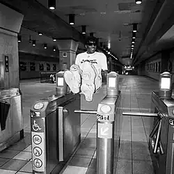 A black-and-white photograph of a man jumping over a turnstile.