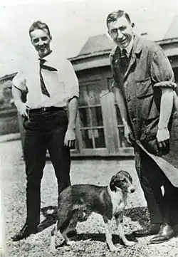Two men standing behind a dog, black and white photo circa 1922