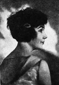 A young woman with light skin and dark hair cut in a short bob, photographed in profile, with her upper back facing the camera
