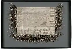 A weathered piece of parchment 20 inches long and 30 1/2 inches wide with faded Latin text in the centre and a 100 signatures around the sides with corresponding wax seals attached.