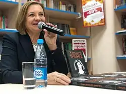 Vavilova speaking into a microphone besides her book, indoors
