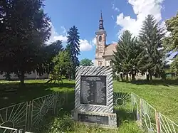 Village centre with World War II memorial and abandoned Serbian Orthodox Church in the background.