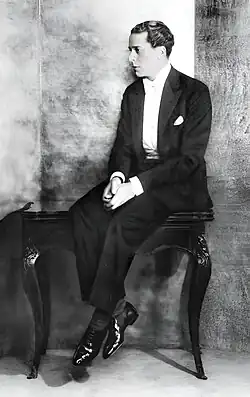 Young white man, clean shaven, perching pensively on a small side table