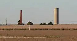 Tall brick chimney and cylindrical concrete water-tower standing alone in cornfield