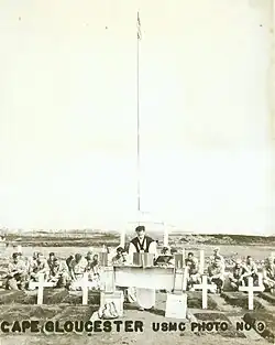 Service personnel with a padre at a memorial service. In the foreground are several graves marked with white crosses.