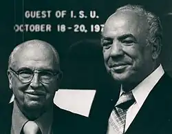 Two men in suits and ties stand for a picture, slightly smiling.