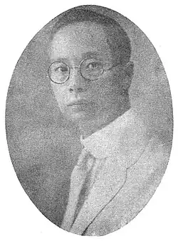 A black-and-white portrait of a thin man in a light suit; he is wearing glasses.