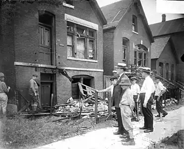 White men and boys standing in front of a vandalized house.