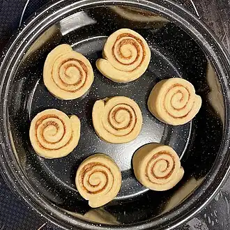 7 raw cinnamon rolls in a round pan, with some space between them to allow for expansion