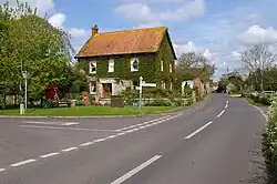 White painted houses with red roofs. In the background is a hill with a tower on it and in the foreground grass and hedgerows