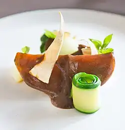 A slice of squash covered with a sauce and garnished with basil sprouts and a tortilla chip.