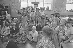 Group of children seated on floor and tables in a classroom.