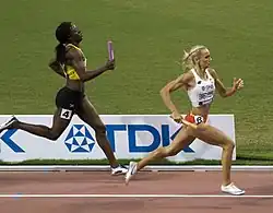 Jackson running with a baton in her hand behind another runner