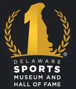 Yellow logo on a black background, map of Delaware with the number "1" superimposed surrounded by a laurel wreath, with "Delaware Sports Museum and Hall of Fame" written underneath