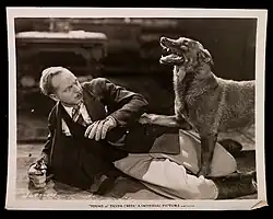 A black and white photograph of a dog standing over a fallen man holding a gun.