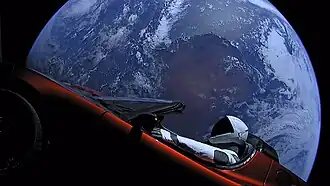 A mannequin (Starman) in a spacesuit drives a car with the Earth in the background