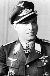 The black and white photo of a man, shown from the front. He wears a military uniform with an Iron Cross displayed at the front of his shirt collar.