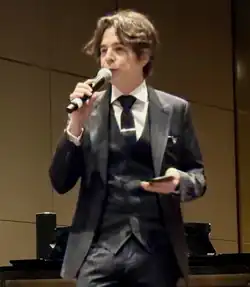 Fernando Garibay is dressing in a suit, and speaking to a microphone