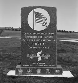 Black-and-white photograph of a large granite memorial. Inscribed are a large United States flag, and below it is text dedicating the monument to Korean War veterans. It includes the dates of the war and a map of Korea.