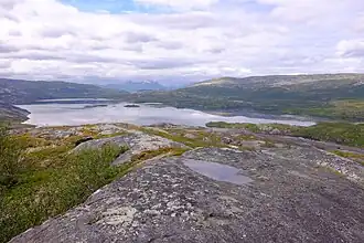 An image of Faulvatnet lake with mountains im the distance and a somewhat cloudy sky