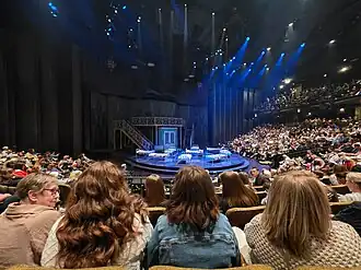 A round stage set up with multiple beds, with the audience surrounding on three sides