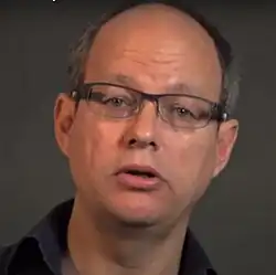slightly blurry close-up of Frank Dikötter wearing a dark shirt, appearing to speak while looking directly at camera