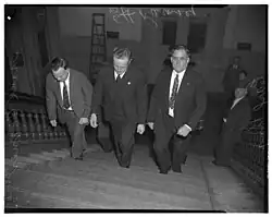 Photo of Earl King, Ernest Ramsay, and Frank Conner in handcuffs walking up staircase of courtroom