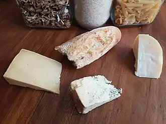 A mixture of cheeses on a wooden cutting board, comprising blue, cheddar and goat gouda, with a loaf of bread
