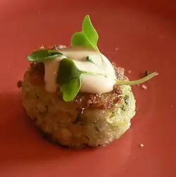 A crabcake with a cream sauce and a garnish of microgreens