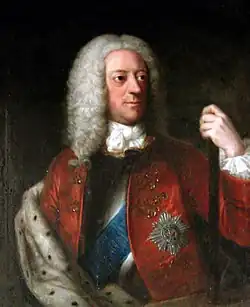 A half-length colour portrait of a man wearing a long wig. Various emblems are apparent on his jacket, and his left hand holds a pole.