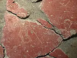 Bright red plaster plate on which a gladiator is drawn and appears in white.
