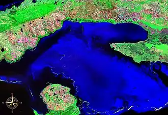 Satellite image of the Gulf of Batabanó, artificially colored blue, with a large land mass above it shaped like a hook, and a smaller landmass below it shaped like a mitten. The land is artificially colored, mostly green with red and pink tracts of land.