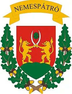 The coat of arms is red, green and yellow. Two animals with swords are depicted on the crest, a green garland borders the crest, a yellow ribbon states the town’s name at the top.