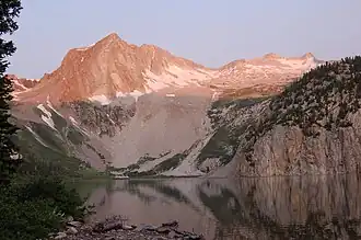 An exposed rock mountain peak and snow covered lower slopes over a Lake