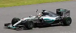 A picture of Lewis Hamilton driving a Mercedes F1 W06 Hybrid formula one car during the 2015 British Grand Prix, raising his arm in celebration after winning the race.
