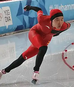 Speed skater Han Mei skating on ice. A blue boundary displaying text related to the 2016 Winter Youth Olympics can be seen in the background.