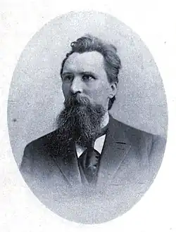 A portrait of a middle-aged German-American man with short hair, a mustache, and a long beard wearing a suit.