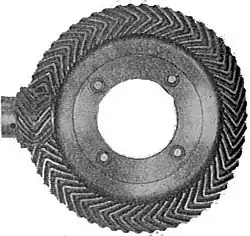 Black-and-white photograph of the side of a metallic wheel with pinions shaped as a wedge. On the left side, the head of an axis ends on a small gear. The edge of the gear rests on the metallic wheel with matching wedge pinions.